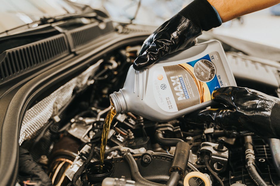 A mechanic wearing gloves pouring oil into a car engine in a garage setting.