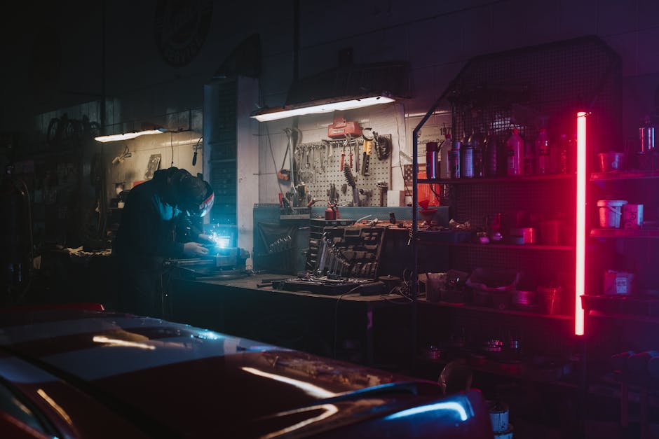 Mechanic working in a dimly lit garage, highlighted by neon lights and tools around.
