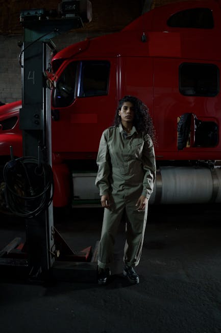 A female auto mechanic standing confidently in a workshop with a red truck in the background.